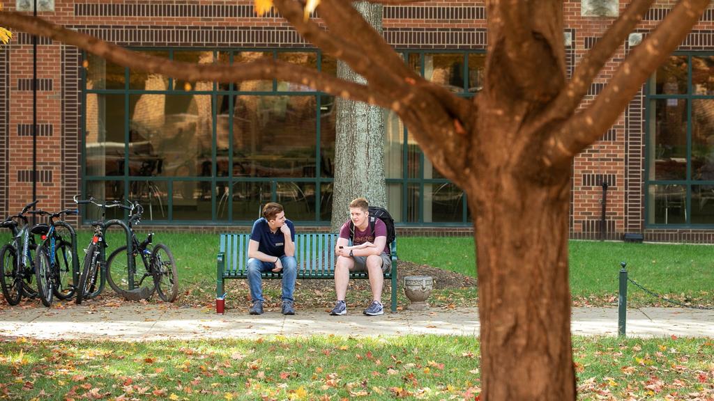 Two students sit on a bench outside the Johnson Center